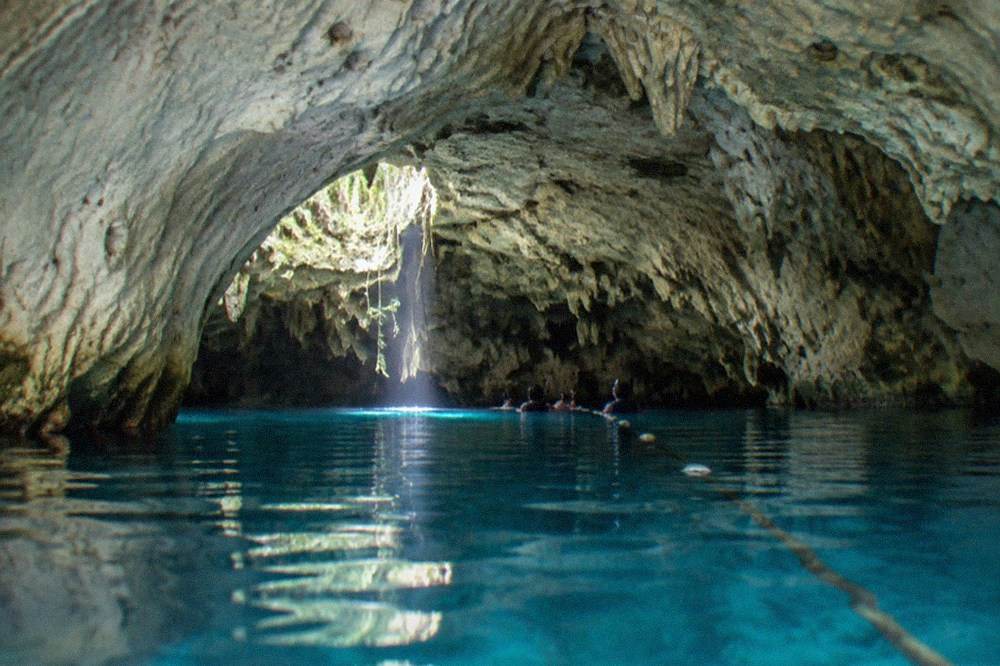 Underwater view of a cavern cenote with pale limestone formations and a shaft of daylight over still clear water