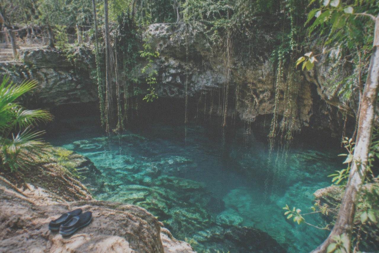 Clear turquoise water in an open jungle cenote surrounded by limestone rock and hanging vines