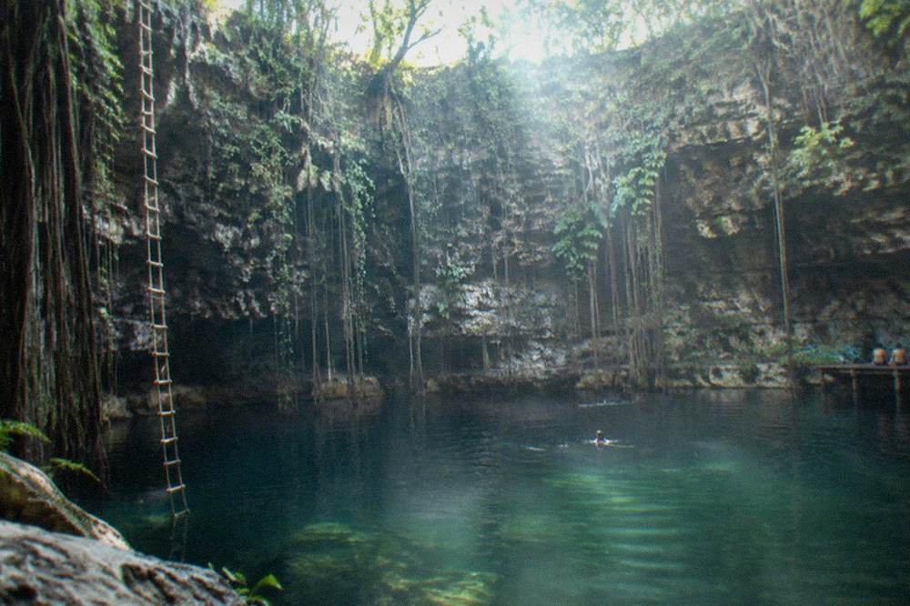 Sunlight beams entering a cavern cenote through an opening above still water
