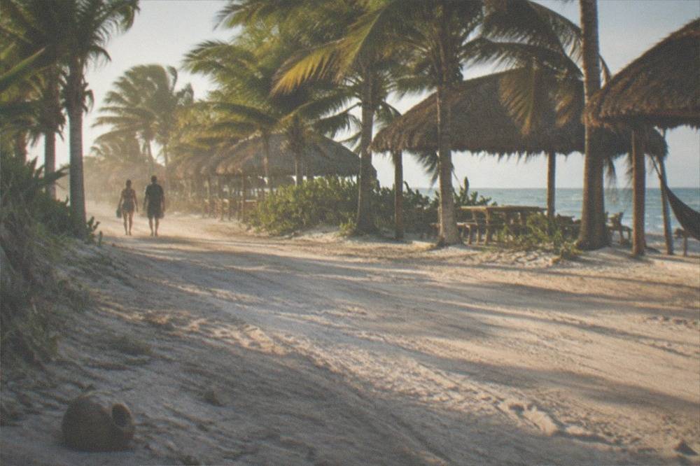 Row of bicycles parked on a sandy road beside palm trees near a cenote entrance