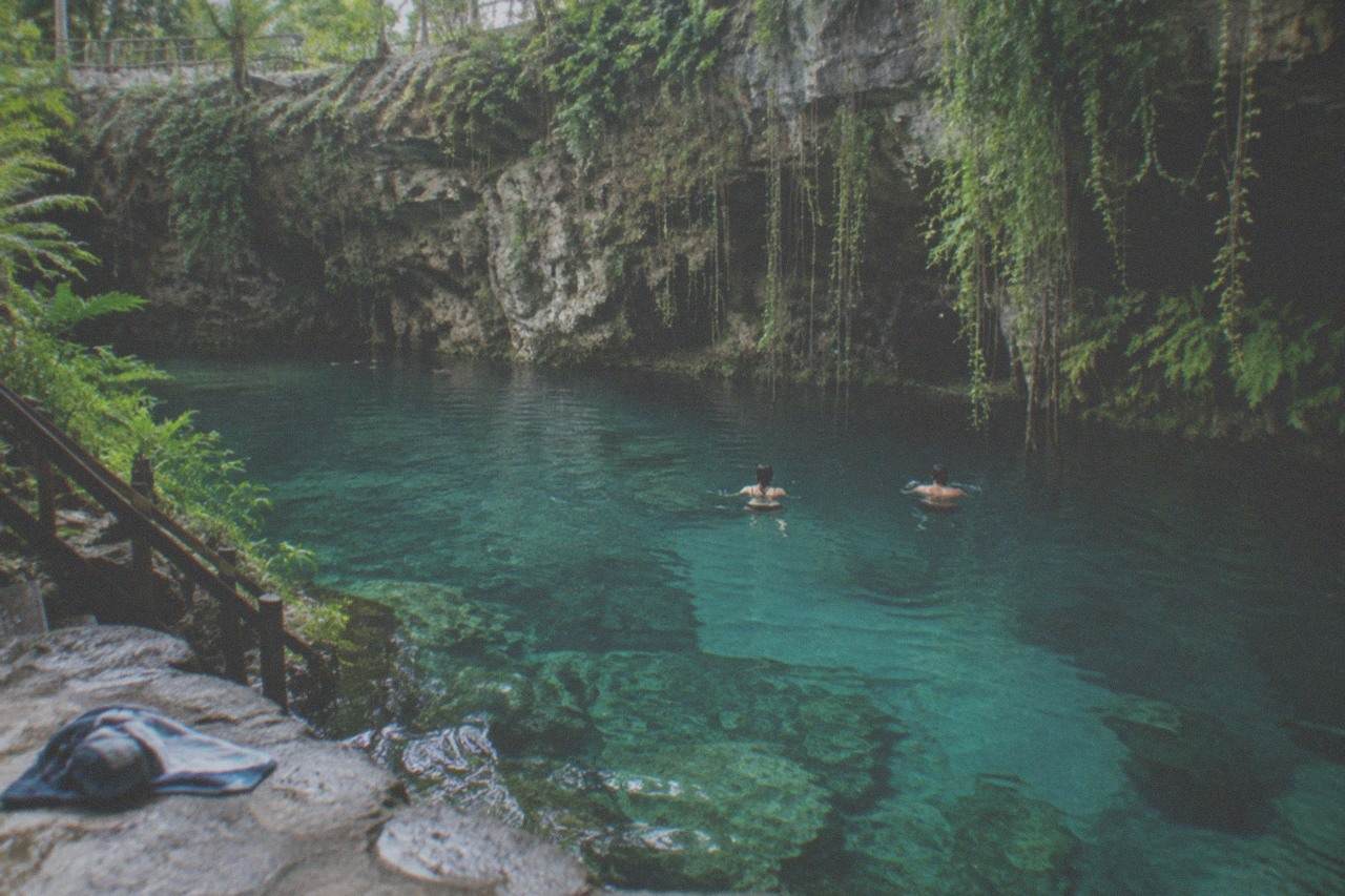 Clear turquoise water in a jungle cenote surrounded by limestone rock and hanging vines