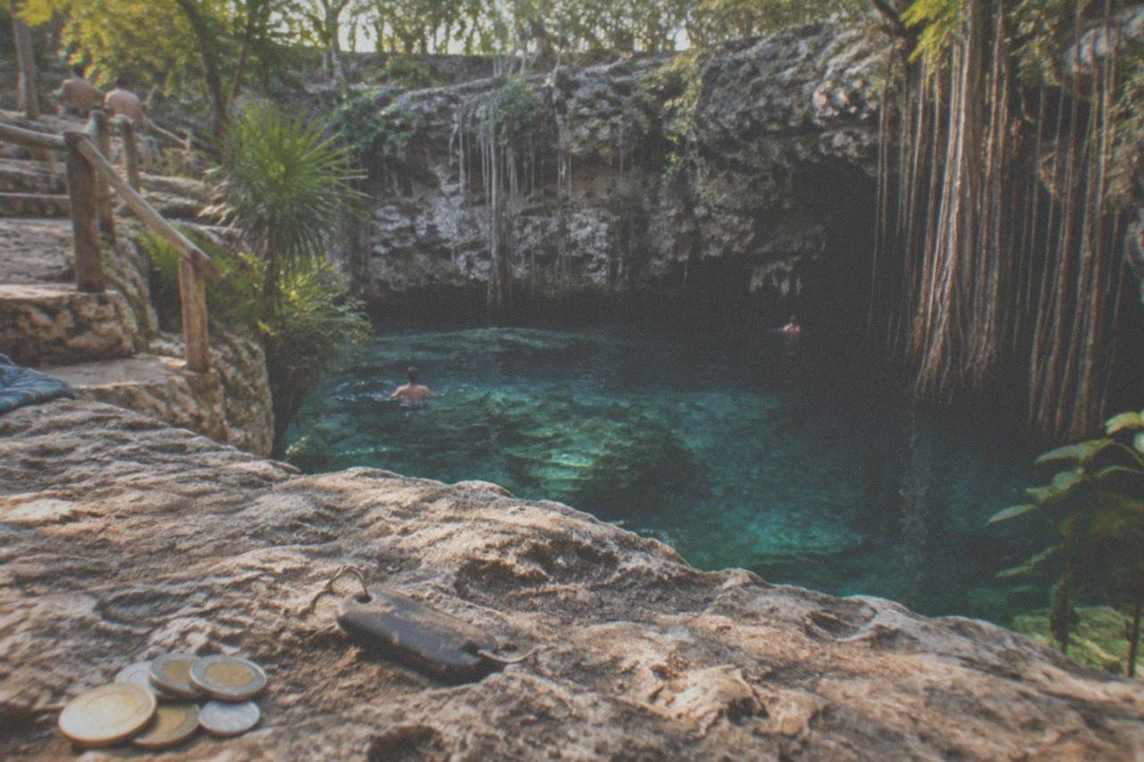 Clear turquoise water in an open limestone cenote surrounded by rock walls and hanging vines