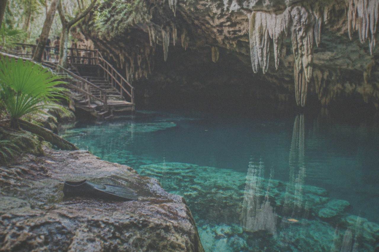 Clear turquoise water filling a limestone cavern opening with stalactites hanging above the surface