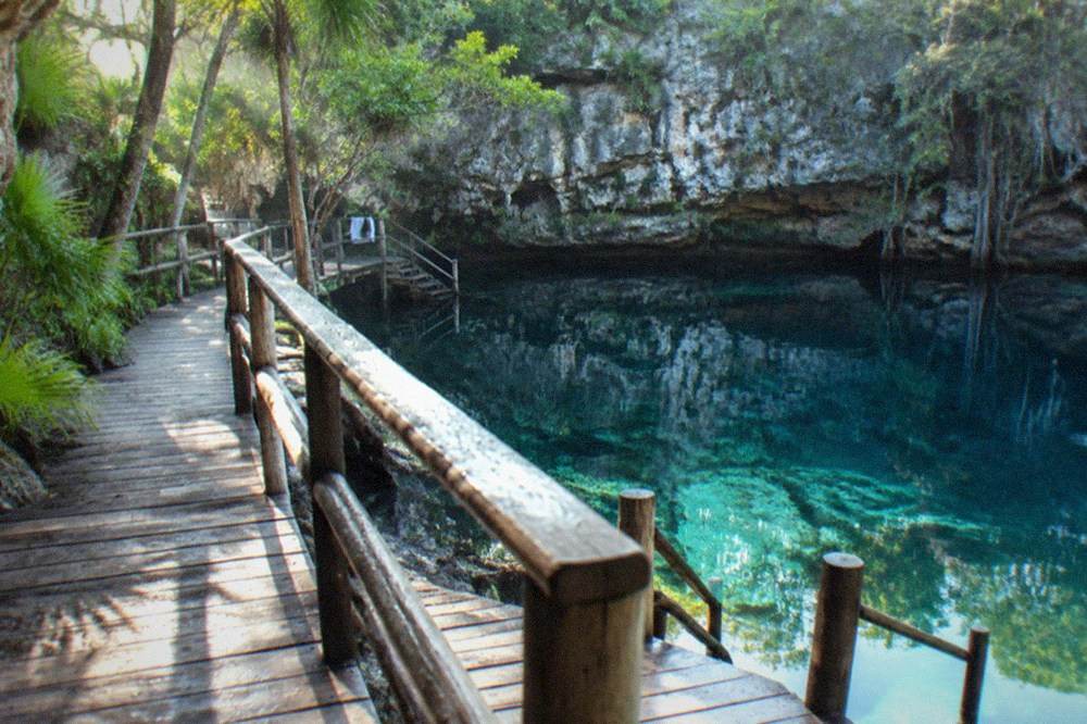 Wooden swim platforms and stairs along a cenote edge under limestone cliffs in morning light