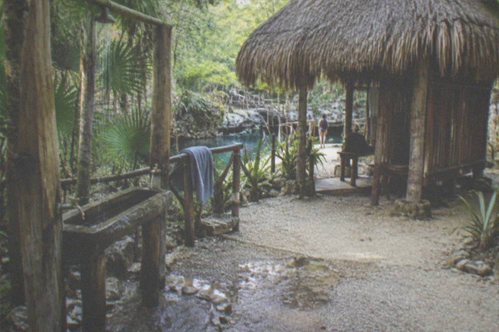 Freshwater rinse station and changing palapa beside a cenote entrance in a jungle clearing