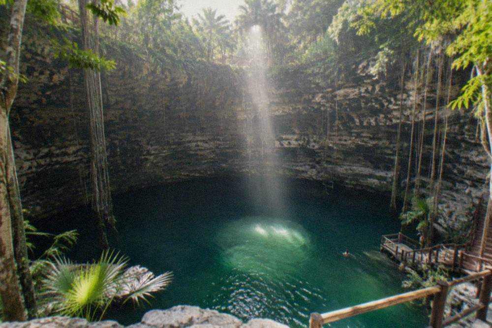 Sunlight shaft falling through a cenote opening onto still water