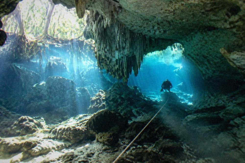 Diver following a guideline through a sunlit limestone cavern passage