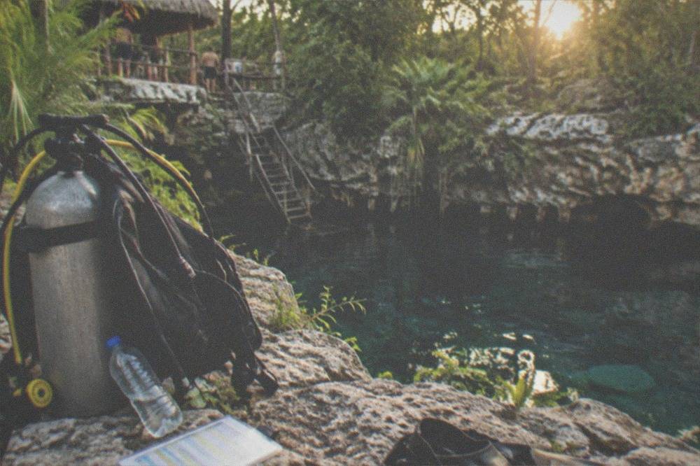 Diver's checklist and scuba gear laid out on rocks beside a cenote