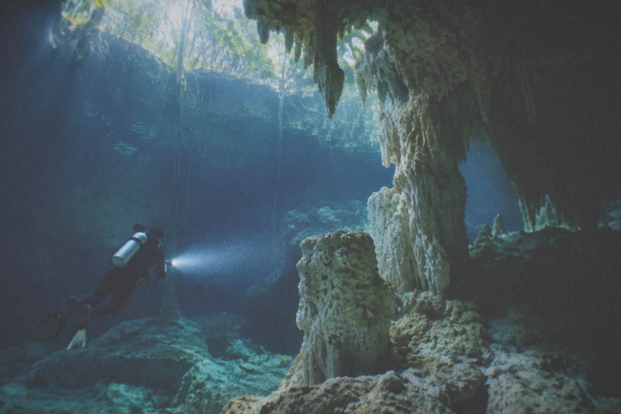 Diver's light beam crossing clear cavern water past limestone formations