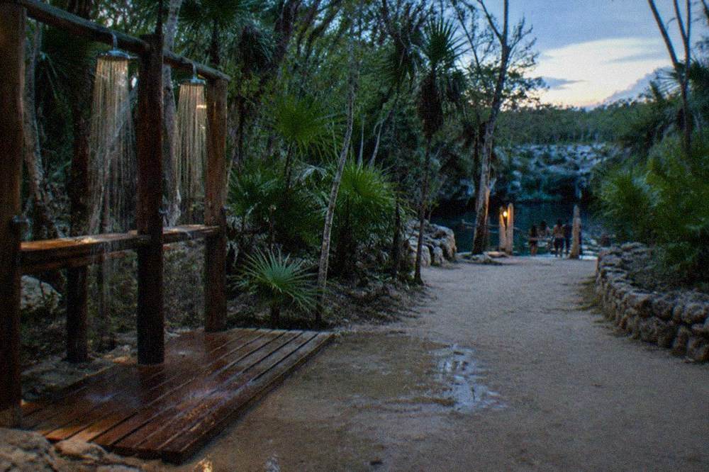 Wooden rinse station with freshwater showers beside a jungle path leading to a cenote