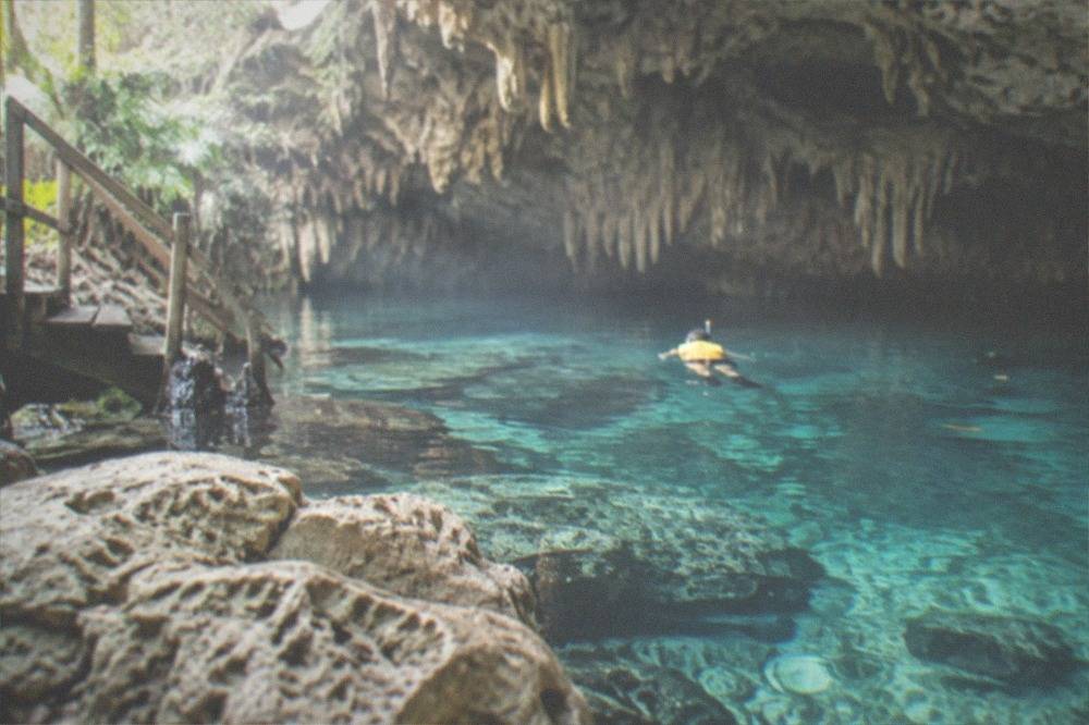 Snorkeler in a life vest floating over clear water past limestone rock formations in a cavern cenote
