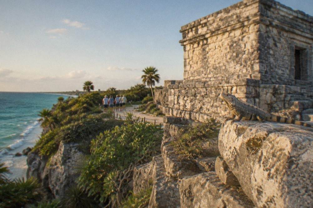 Weathered Mayan stone temple against a clear sky with turquoise sea visible beyond the cliff