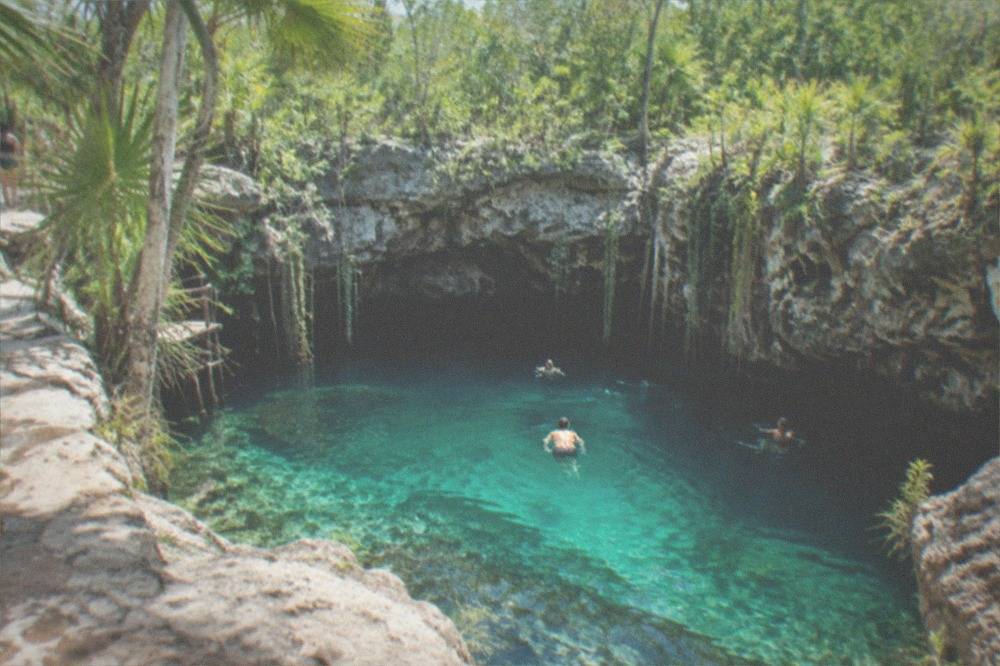 Clear turquoise water of a jungle cenote surrounded by limestone rock and hanging vines