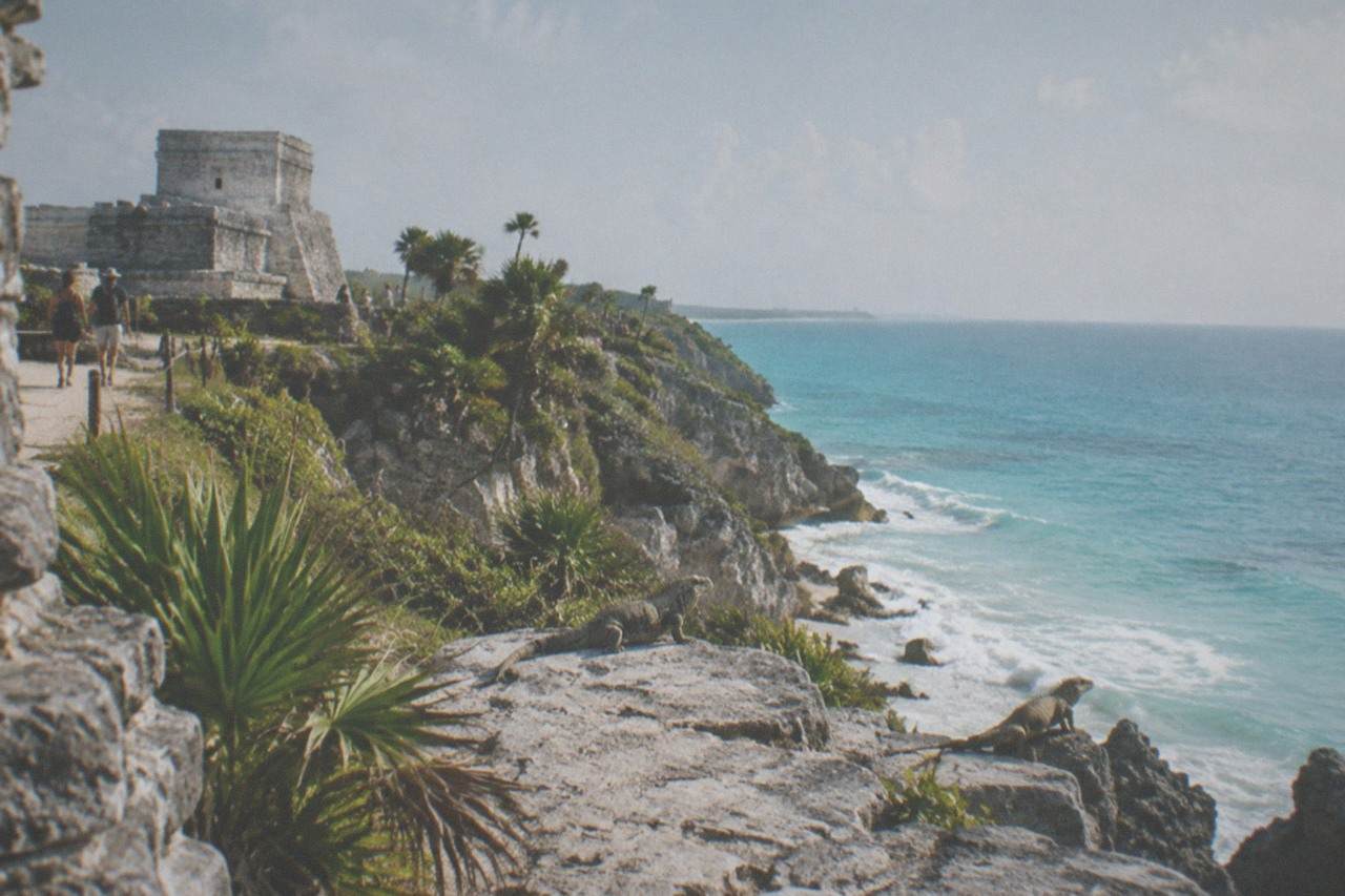 Ancient stone walls of a cliffside Mayan ruin overlooking a turquoise Caribbean Sea under a bright sky