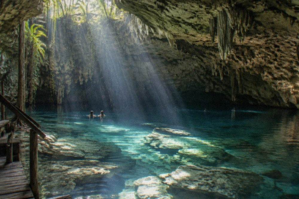 Sunlight beams entering a flooded limestone cavern over pale rock formations underwater