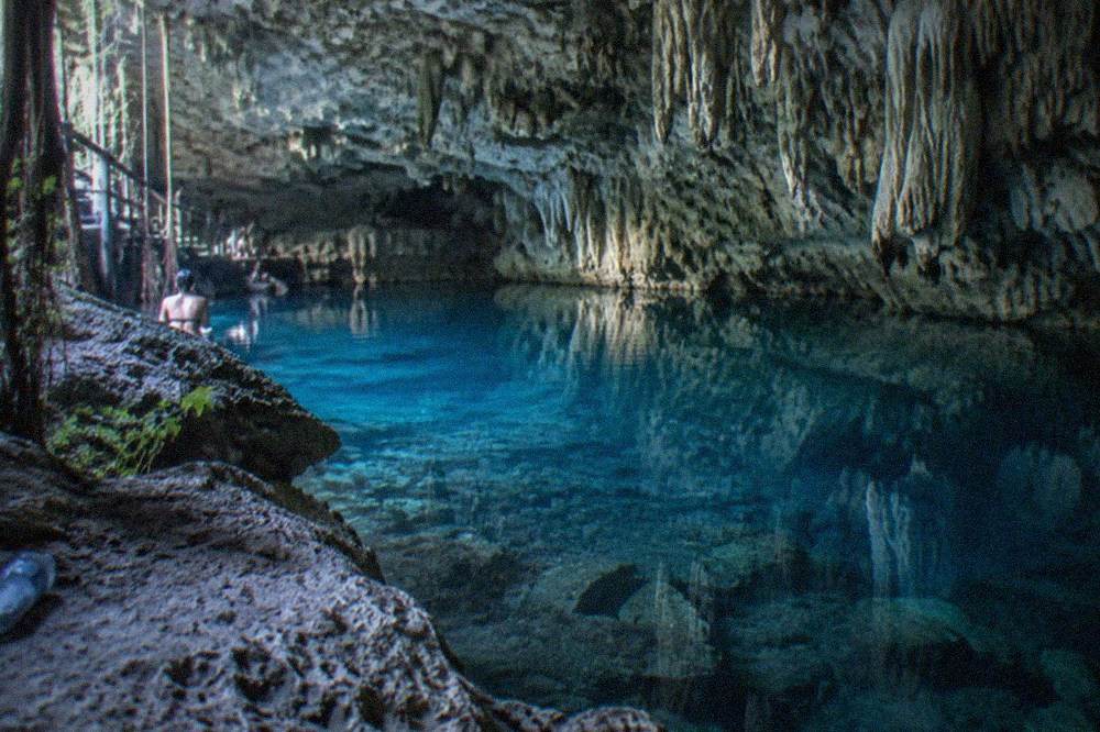 A limestone cavern interior with still clear water reflecting rock walls and hanging formations