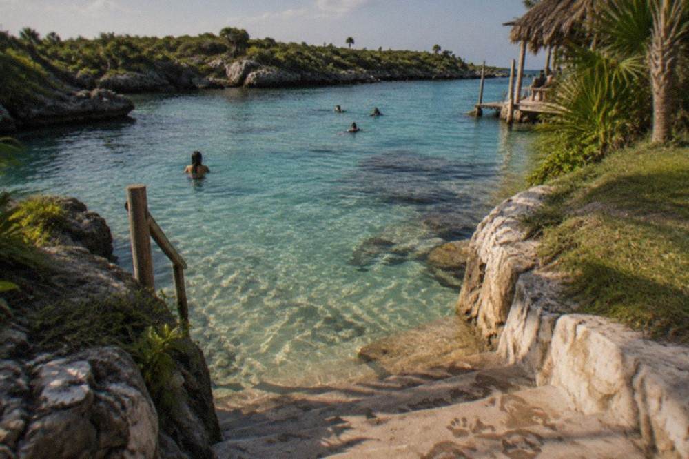 Shallow clear water in an open cenote with stone steps leading down to a gentle swimming area