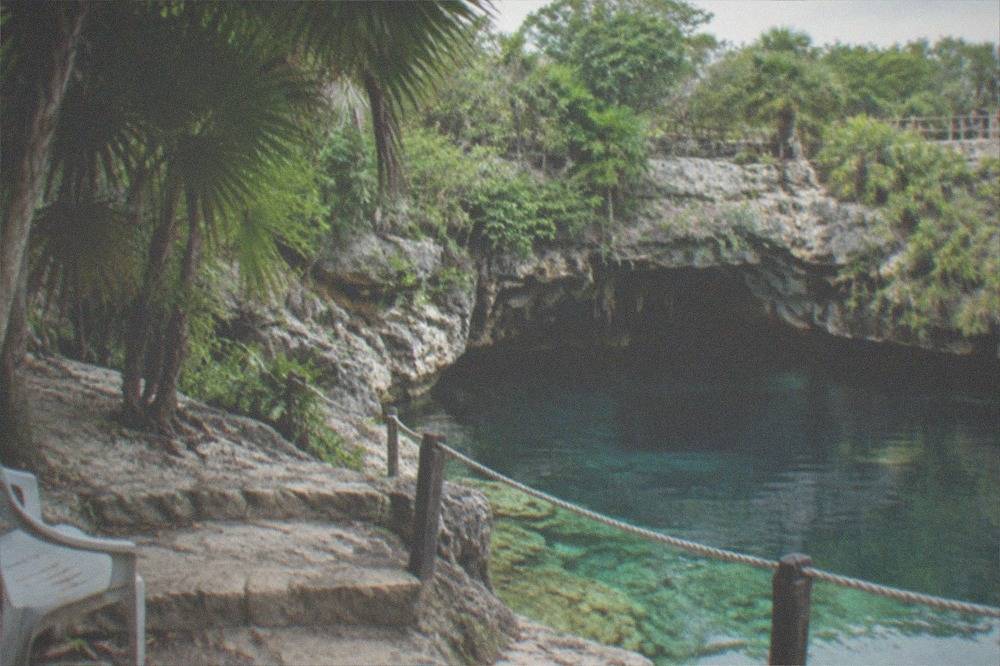Limestone steps beside a calm shallow cenote with rope boundary and shaded sitting area