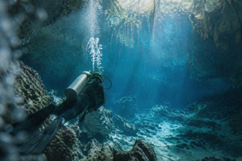 A certified diver descending into the cavern zone of a clear Tulum-area cenote