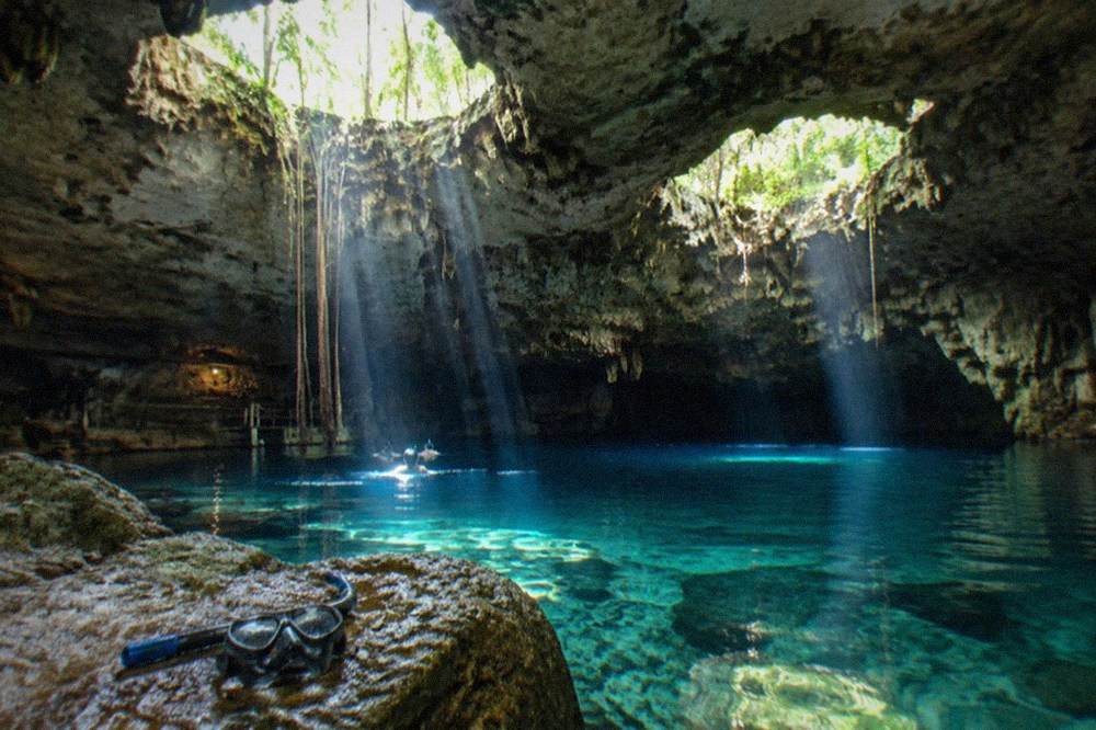 Two circular limestone openings filled with clear blue water connected by a cavern interior