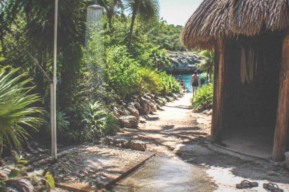 A freshwater rinse shower station and wooden changing area beside a cenote entrance path