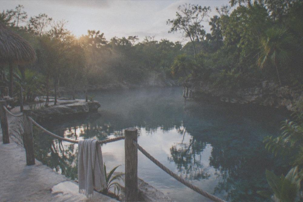 A calm empty jungle pool at first light with wooden decking and rope rail along the edge
