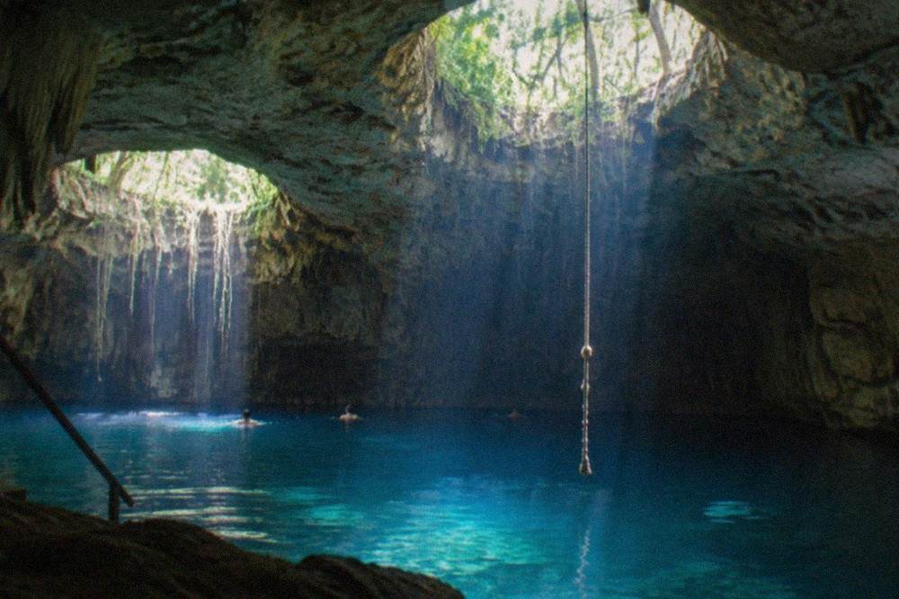 Circular openings in limestone letting daylight beams into turquoise water