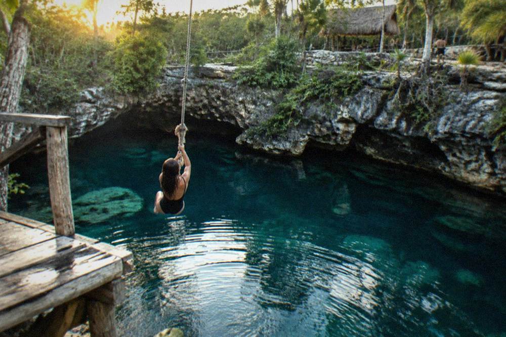 Wooden platform and rope swing above deep turquoise sinkhole water