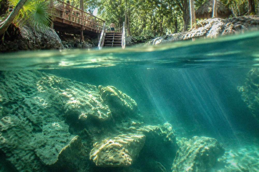 Sunlight beaming through clear green water onto submerged limestone rocks