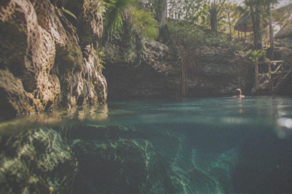 A snorkeler's view of sunlit limestone walls above and below clear water