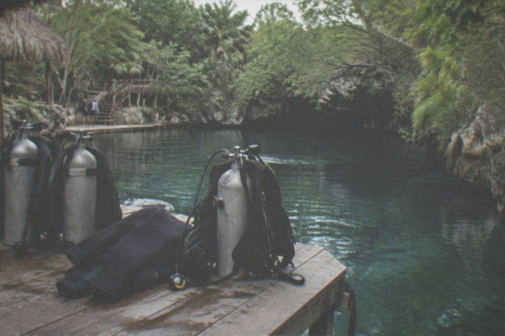 Scuba tanks and dive gear resting on a wooden deck beside a calm jungle cenote