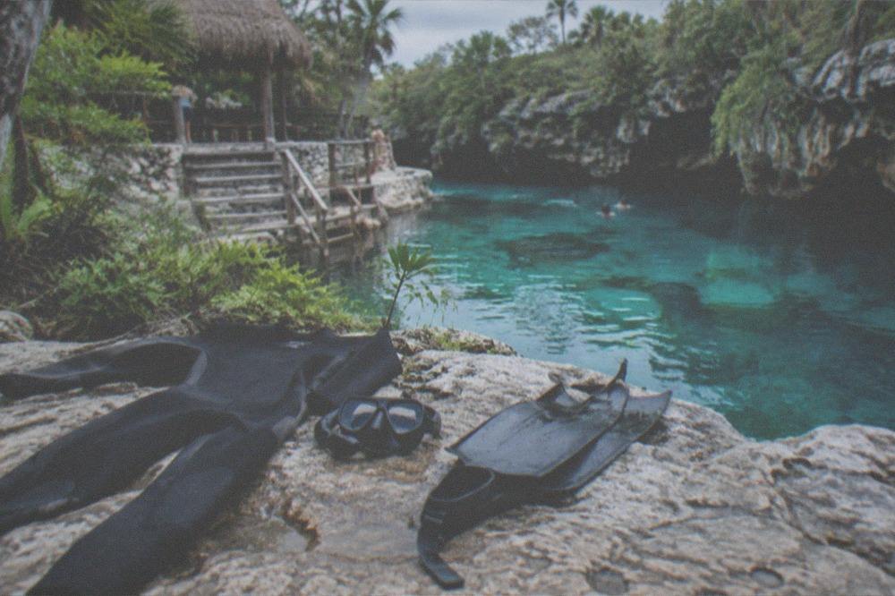 A wetsuit, mask and fins laid out on a rocky ledge beside turquoise cenote water