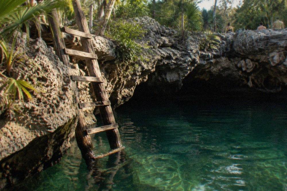 Limestone rock opening above clear green water with wooden ladder descending