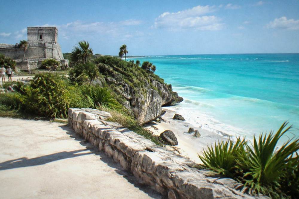 Stone Maya ruin walls on a cliff above a wide turquoise sea
