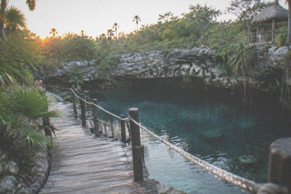 Wooden walkway and railing leading down to a round open cenote pool