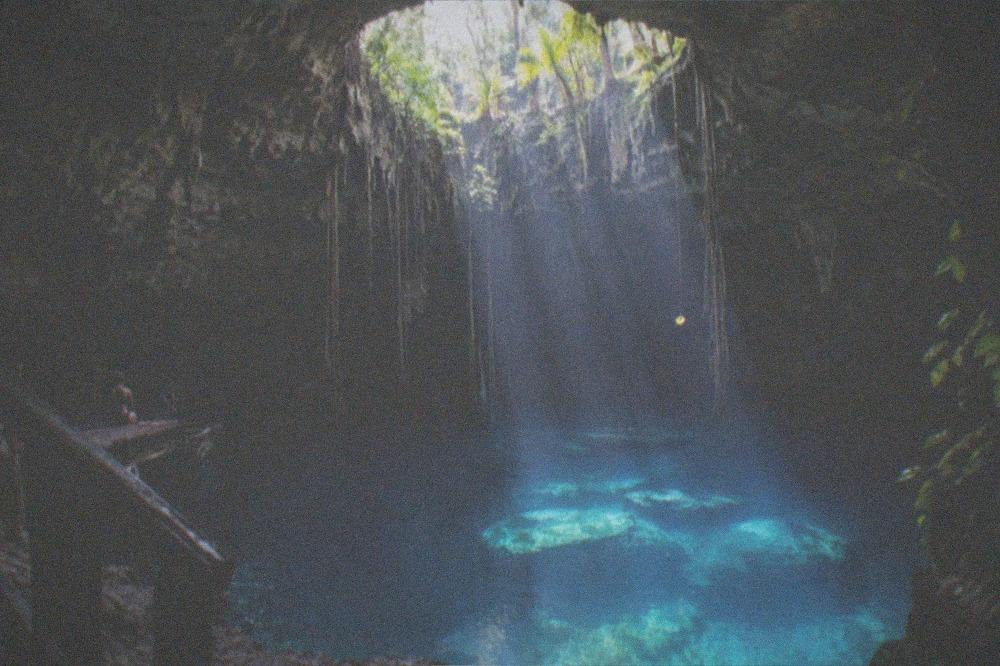 Sunlight beams falling through a round opening onto still blue cave water