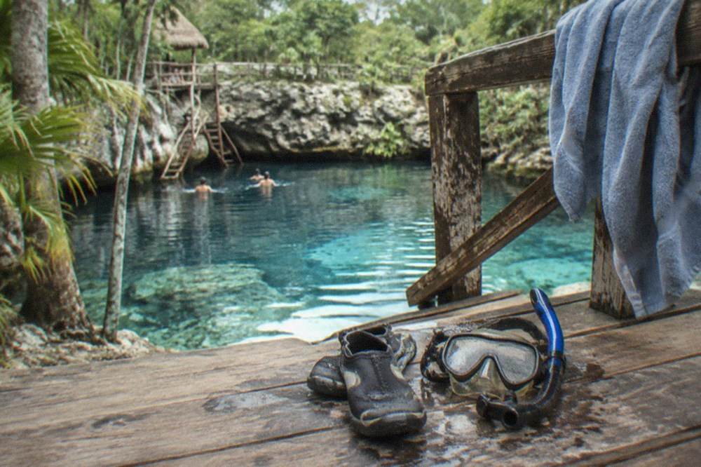 Water shoes and a snorkel mask drying on a wooden deck beside a cenote entrance