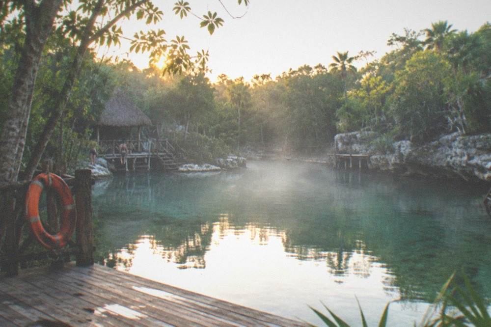 Morning light hitting the surface of a calm open cenote with empty wooden decks