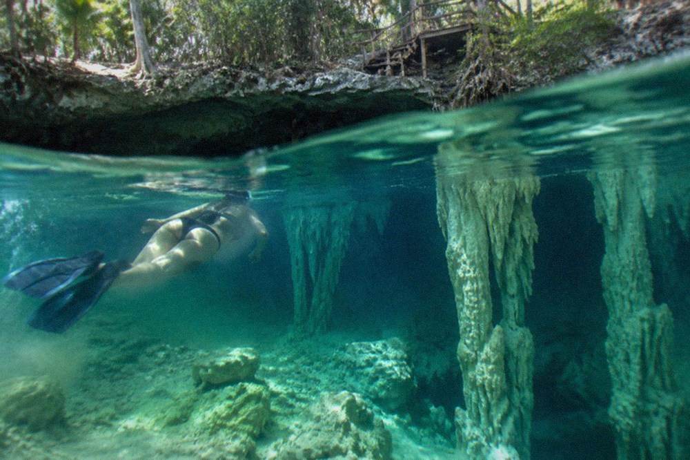 Snorkeler floating above submerged stalactite columns in very clear water