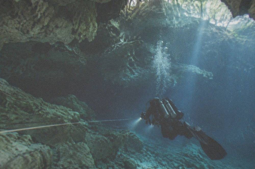 Diver with twin lights following a guideline through a lit limestone cavern passage