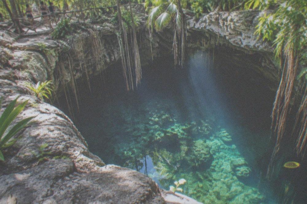 Midday sunbeams entering a circular sinkhole opening above still clear water