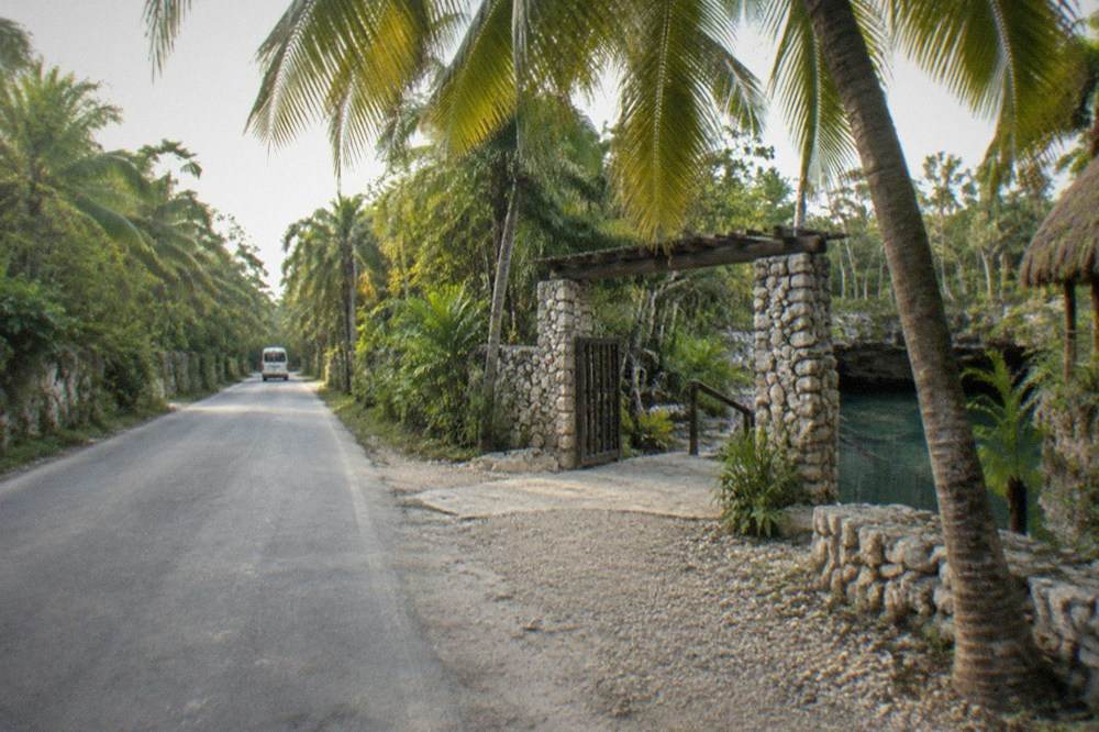 A quiet jungle road running toward a cenote entrance with bicycles leaning on a fence
