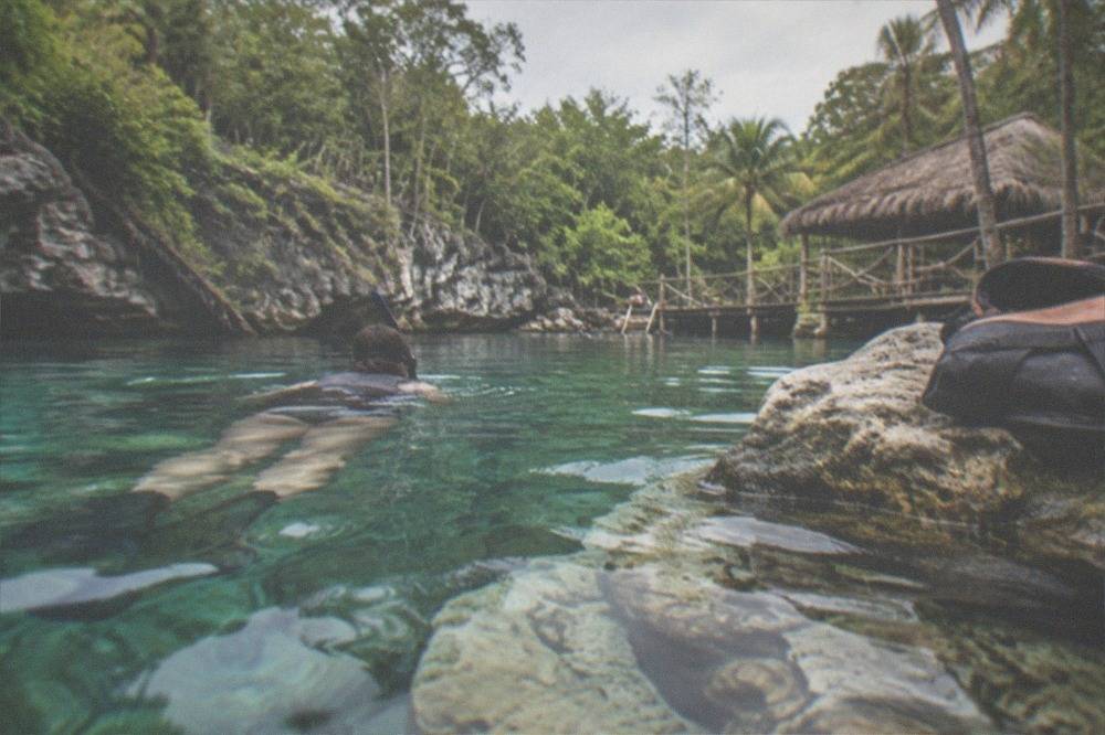 A snorkeler floating over pale limestone formations in clear shallow cenote water