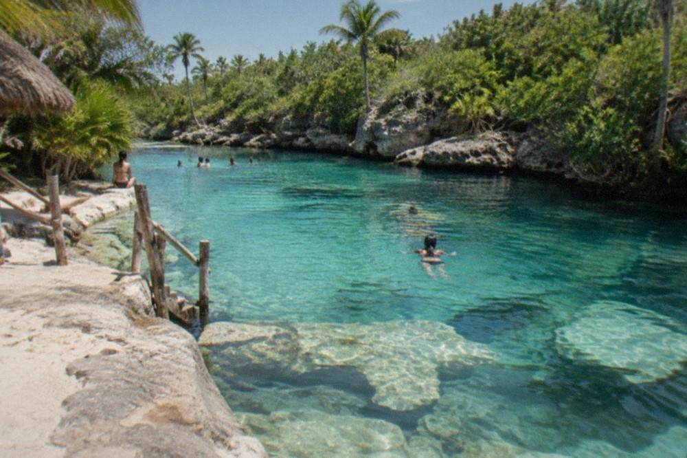 Shallow turquoise cenote water with limestone rock formations visible beneath the surface