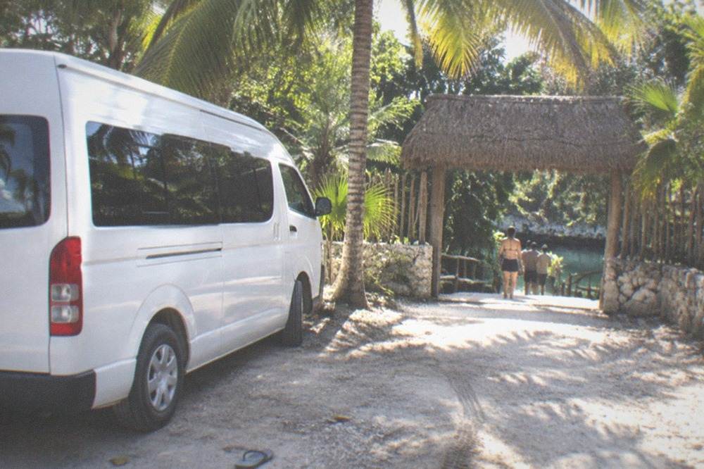 Tour van parked on a jungle roadside near a cenote entrance