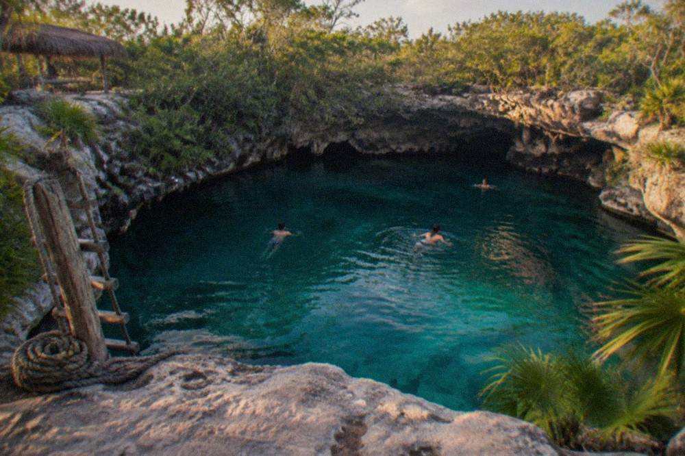 Turquoise water filling a limestone sinkhole surrounded by jungle vegetation