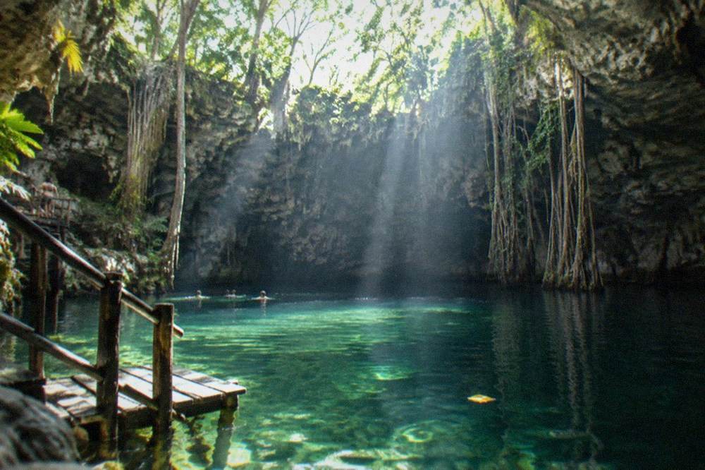 Open cave ceiling with sunlight beaming onto clear green water