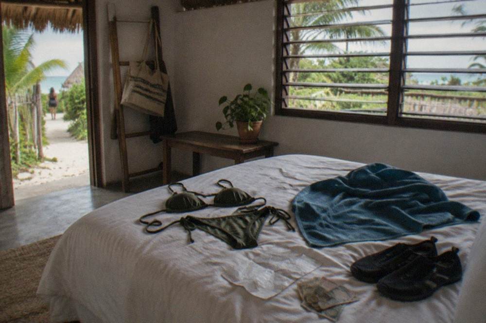A packing checklist with swimwear, towel and water shoes laid out on a bed