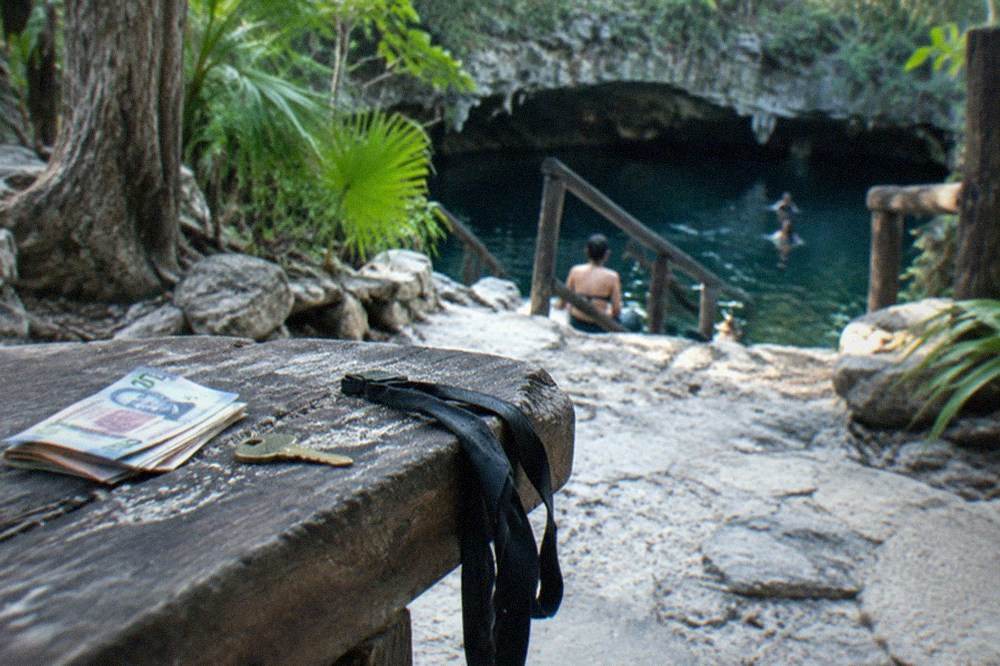 A stack of Mexican peso notes and a locker key on a wooden bench by a cenote entrance