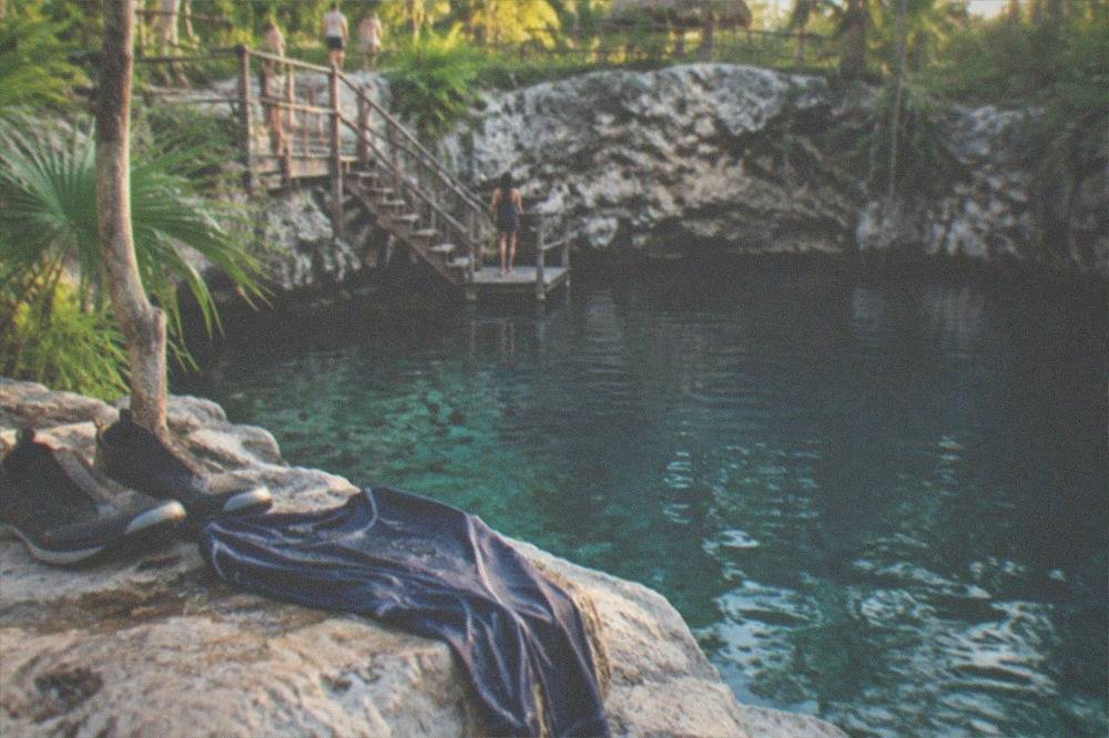 A pair of water shoes and a rash guard drying on a limestone ledge beside turquoise water